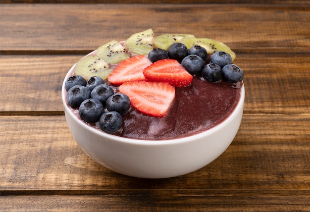 Brasilianische typische Acai-Schüssel mit Kiwi, Blaubeere und Erdbeere über Holztisch.