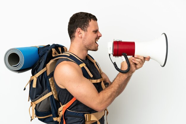 Brasilianischer Bergsteiger mit einem großen Rucksack über isoliertem weißem Hintergrund, der durch ein Megaphon schreit