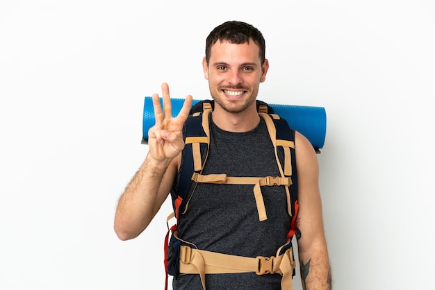 Brasilianischer Bergsteigermann mit einem großen Rucksack über isoliertem weißem Hintergrund glücklich und zählt drei mit den Fingern