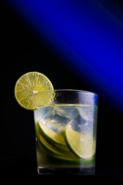 Brasilianischer Cocktail namens Caipirinha. Mit Zitrone, Eis und Cachaça auf dunklem Hintergrund mit Blaulicht. Platz kopieren