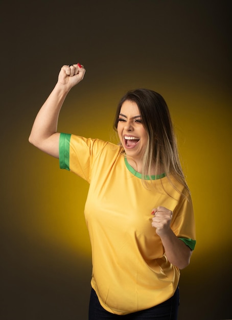 Brasilianischer Fan Brasilianischer Frauenfan, der im Fußball- oder Fußballspiel auf gelbem Hintergrund feiert Brasilien-Farben