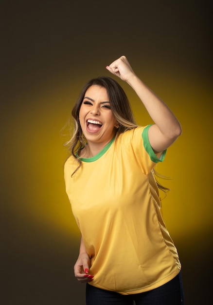 Brasilianischer Fan Brasilianischer Frauenfan, der im Fußball- oder Fußballspiel auf gelbem Hintergrund feiert Brasilien-Farben