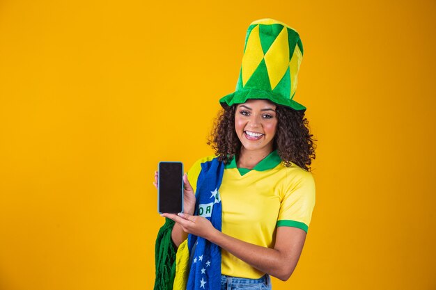 Brasilianischer Fan, der ein Smartphone mit Kopienraum hält. brasilianische Unterstützerin mit Handy mit weißem Bildschirm zum Schreiben von Text.