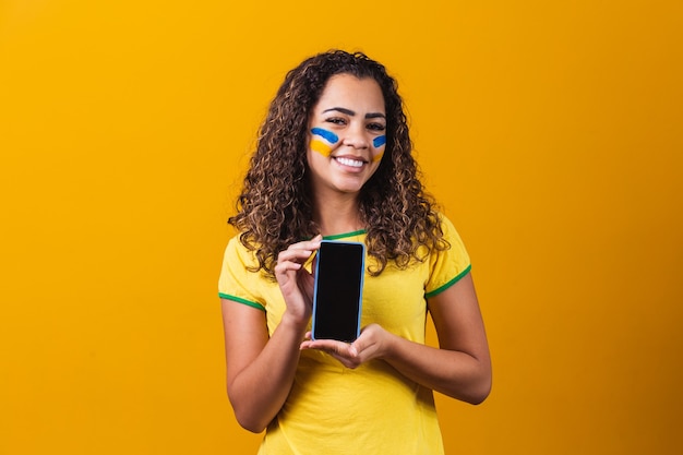 Brasilianischer Fan, der ein Smartphone mit Kopienraum hält