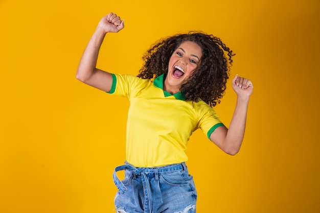 Brasilianischer Fan. Springen, um zu feiern, brasilianischer Fan, der Fußball- oder Fußballspiel auf gelbem Hintergrund feiert. Farben Brasiliens.