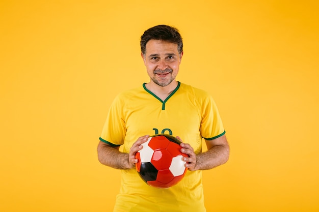 Brasilianischer Fußballfan mit gelbem Trikot und Retro-Ball in den Händen