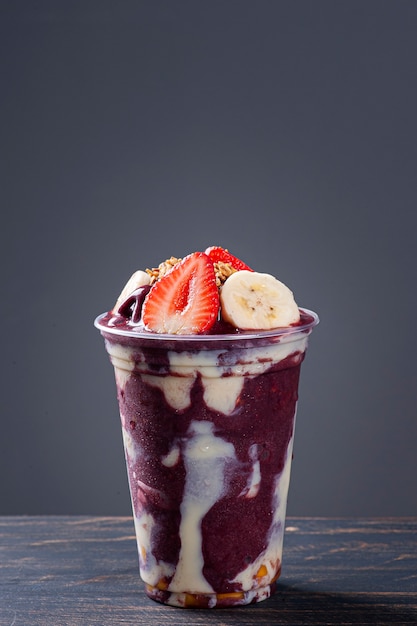 Brasilianischer gefrorener Açaí in einem Plastikbecher mit Kondensmilch, Banane und Erdbeere. Obst aus dem Amazonas.