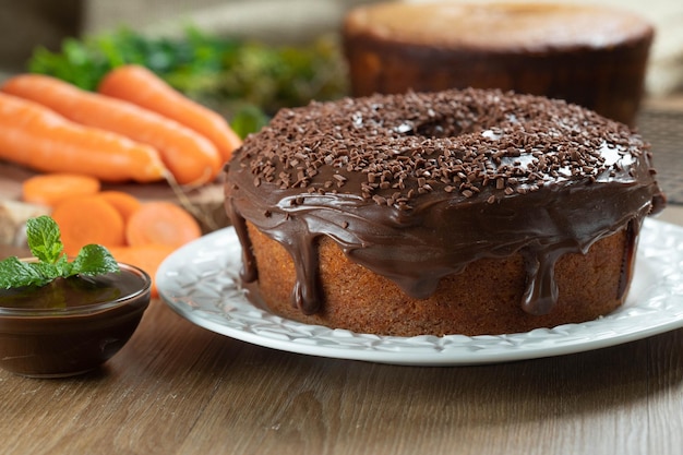 Brasilianischer Karottenkuchen mit Schokoladenglasur auf Holztisch mit Karotten im Hintergrund