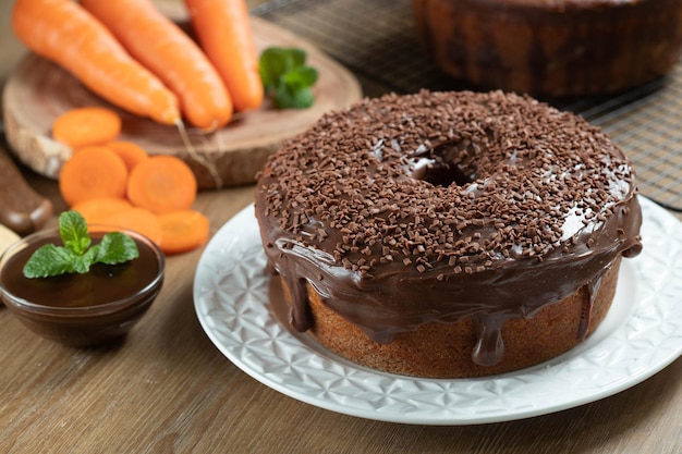 Brasilianischer Karottenkuchen mit Schokoladenglasur auf Holztisch mit Karotten im Hintergrund