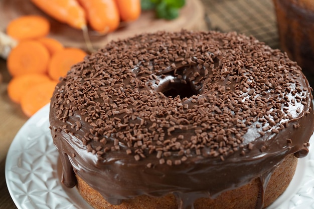 Brasilianischer Karottenkuchen mit Schokoladenglasur auf Holztisch mit Karotten im Hintergrund