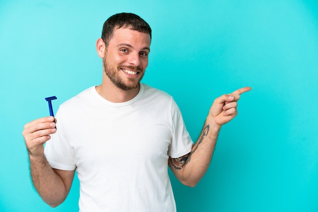 Brasilianischer Mann, der seinen Bart isoliert auf blauem Hintergrund rasiert und mit dem Finger zur Seite zeigt