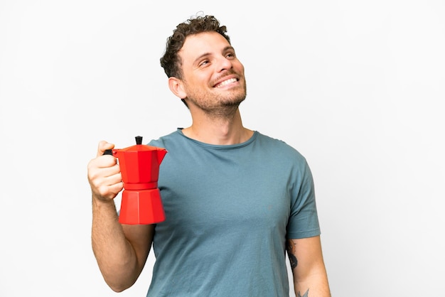 Brasilianischer Mann mit Kaffeekanne vor isoliertem weißem Hintergrund, der lächelnd nach oben schaut