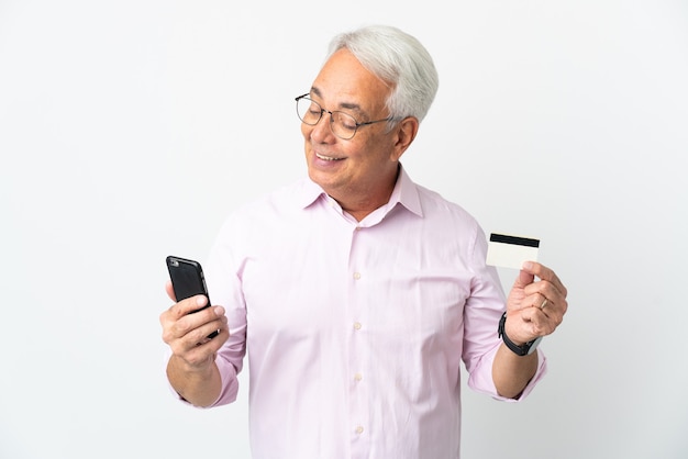 Brasilianischer Mann mittleren Alters lokalisiert auf weißem Hintergrund, der mit dem Handy mit einer Kreditkarte kauft