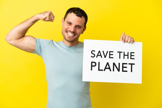 Brasilianischer Mann über isoliertem lila Hintergrund, der ein Plakat mit dem Text "Save the Planet" hält und eine starke Geste macht