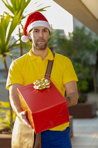 Brasilianischer Postbote verkleidet als Weihnachtsmann, der ein Geschenk liefert. Online-Kauf wird geliefert.