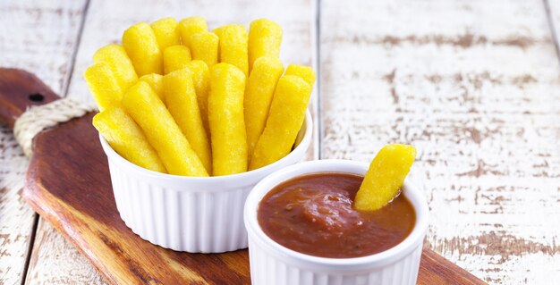 Brasilianischer Snack namens Polenta, serviert mit Sauce und Ketchup, isolierte weiße Oberfläche.