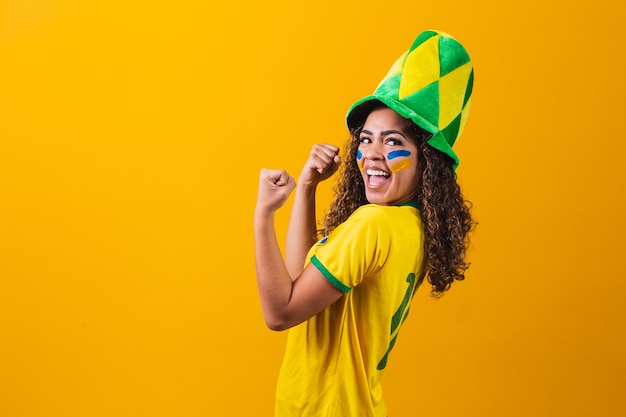 Brasilianischer Unterstützer. Brasilianischer Frauenfan, der auf Fußball- oder Fußballspiel auf gelbem Hintergrund feiert. Brasilien farben. Jawohl!