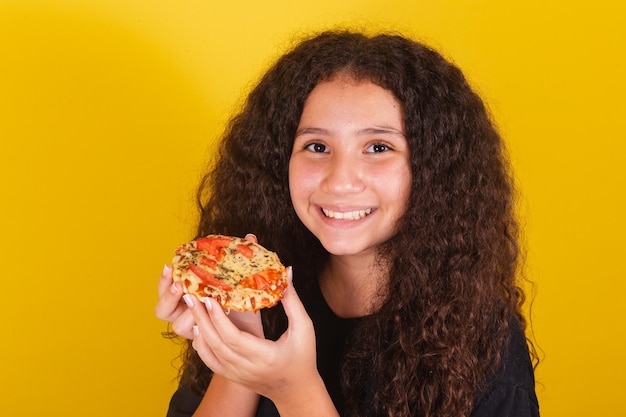 Brasilianisches lateinamerikanisches Mädchen für Afro-Haare mit gelbem Hintergrund, das sich bereit macht, köstliche Mini-Pizza Pizza Margarita-Pizza-Käse, der Käse ausdehnt, zu mondern