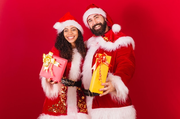 Brasilianisches paar gekleidet für weihnachten weihnachtsmann mama claus tauschen geschenke genehmigte schwarze frau und kaukasischen mann aus