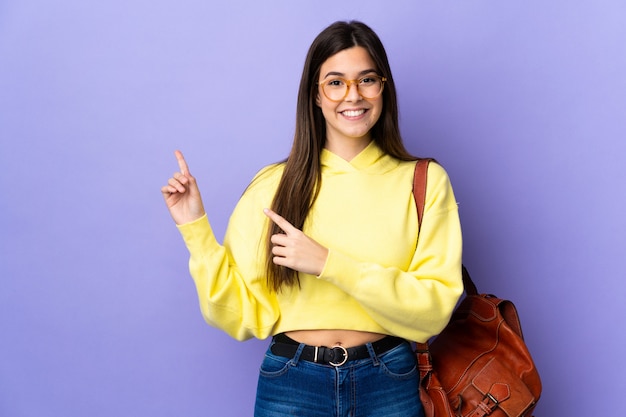 Brasilianisches Studentenmädchen des Teenagers über der isolierten lila Wand, die Finger zur Seite zeigt