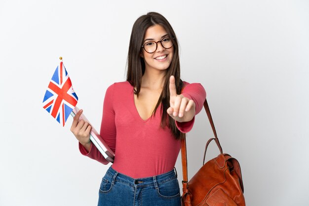 Brasilianisches Teenager-Mädchen, das eine britische Flagge lokalisiert auf weißer Wand hält, die einen Finger zeigt und anhebt