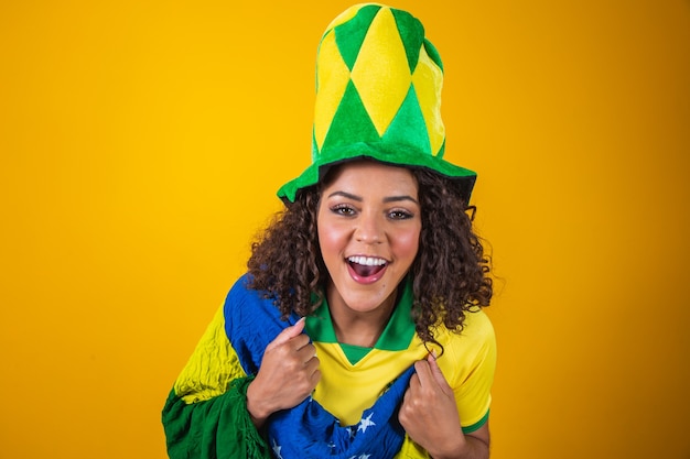 Brasilien-Anhänger. Brasilianischer Frauenfan mit lockigem Haar, der auf Fußball feiert, Fußballspiel auf gelbem Hintergrund. Brasilien farben.