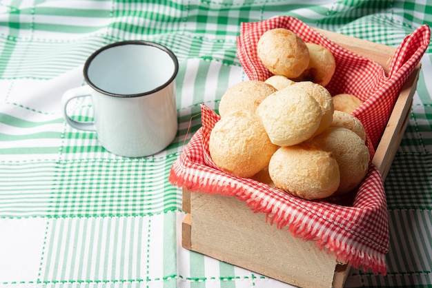 Brasilien Käsebrot, Schachtel mit Käsebrötchen und eine Tasse auf einer grün karierten Tischdecke, selektiver Fokus.