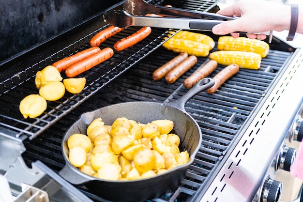 Braten kleiner goldener Kartoffeln in einer Gusseisenpfanne und einem Gasgrill im Freien.