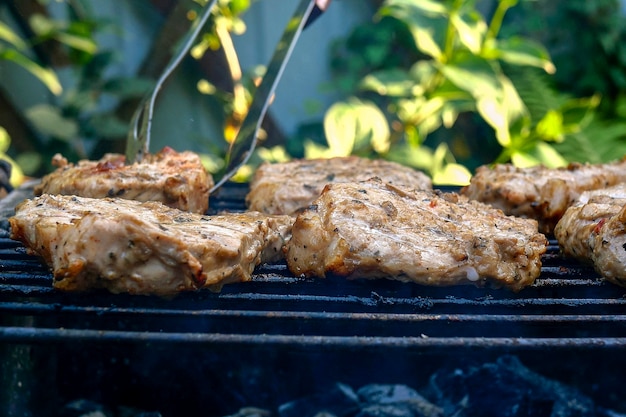 Braten saftige Stücke von frischem Schweinenackensteakfleisch, das auf Grill oder Grillgitter im Freien im Hinterhof zubereitet wird. Auf Holzkohle rauchen. Selektiver Fokus. Nahaufnahme. Draußen.