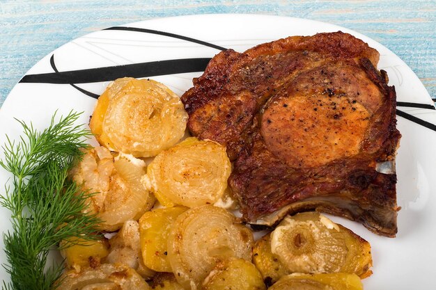 Braten Sie Fleisch mit Kartoffeln und Zwiebeln auf Teller auf blauem Holzhintergrund