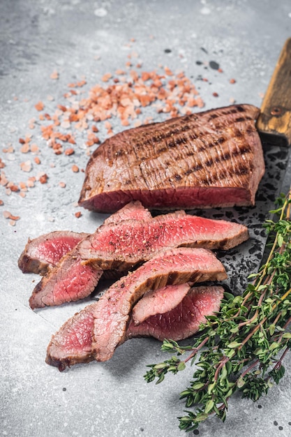 Braten Sie in Scheiben geschnittenes Flank- oder Flap-Steak auf einem Metzgererbeil mit Thymian und rosa Salz Grauer Hintergrund Draufsicht