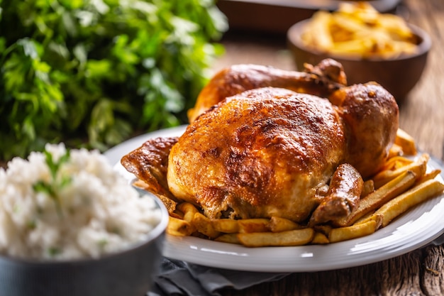 Brathähnchen ganz auf einem Holzbrett mit Beilagenreis und Pommes frites.