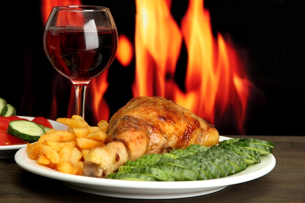 Brathähnchen mit Pommes frites und Gurken, Glas Wein auf Holztisch an der Feuerwand