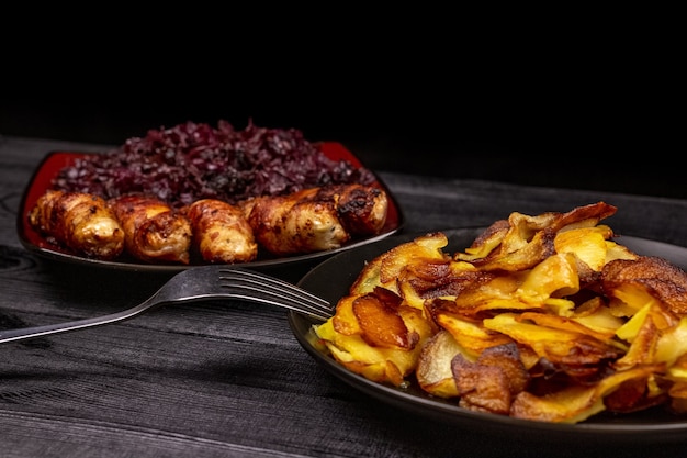 Bratkartoffeln und hausgemachte gegrillte Würstchen oder Chevapchichi mit gedünstetem saurem Rotkohl auf rustikalem Holzhintergrund. Ansicht von oben.