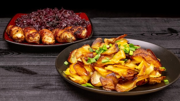 Bratkartoffeln und hausgemachte gegrillte Würstchen oder Chevapchichi mit gedünstetem saurem Rotkohl auf rustikalem Holzhintergrund. Ansicht von oben.