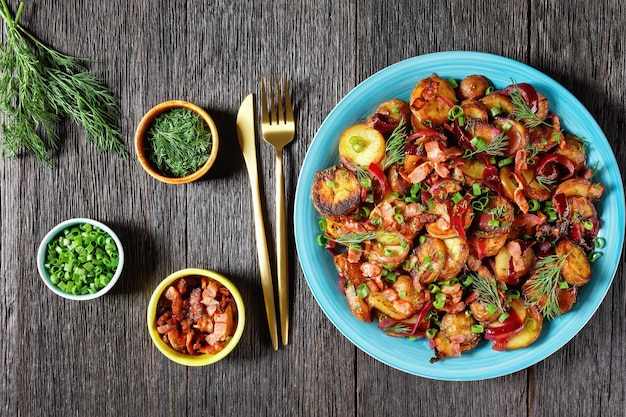 Bratkartoffelsalat ensalada de patata asada con cebolla roja y tocino en un plato azul sobre una mesa de madera rústica oscura cocina alemana plana espacio libre