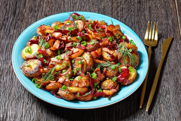 Bratkartoffelsalat ensalada de patata asada con cebolla roja y tocino en un plato azul sobre una mesa de madera rústica oscura cocina alemana