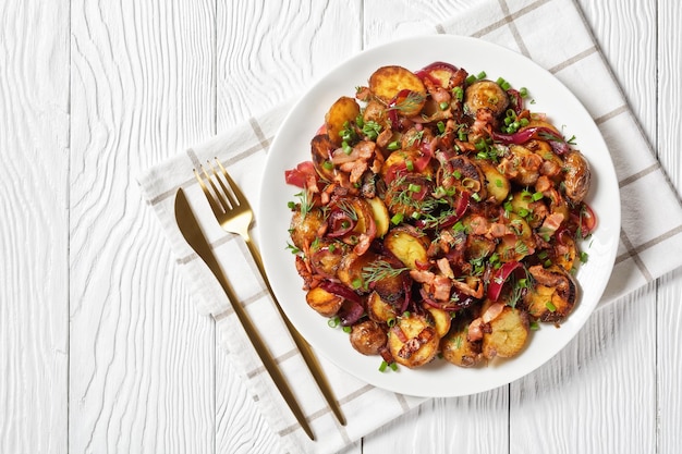 Bratkartoffelsalat ensalada de patata asada con cebolla roja y tocino en un plato blanco sobre una mesa de madera plana espacio libre cocina alemana