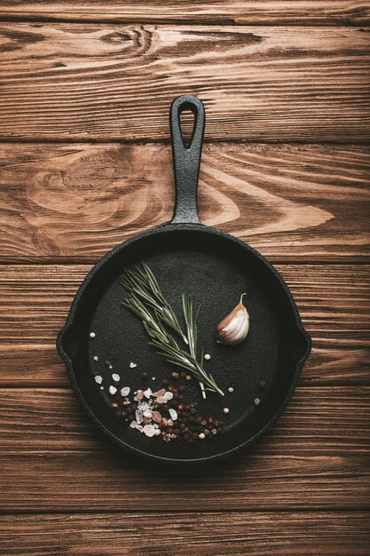 Bratpfanne aus schwarzem Gusseisen mit Zutaten zum Kochen, frischem Rosmarin, Knoblauch, Salz und Pfeffer