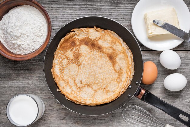 Bratpfanne mit köstlichen Crepes und Zutaten zum Kochen auf einem rustikalen Holztisch dünne Pfannkuchen in