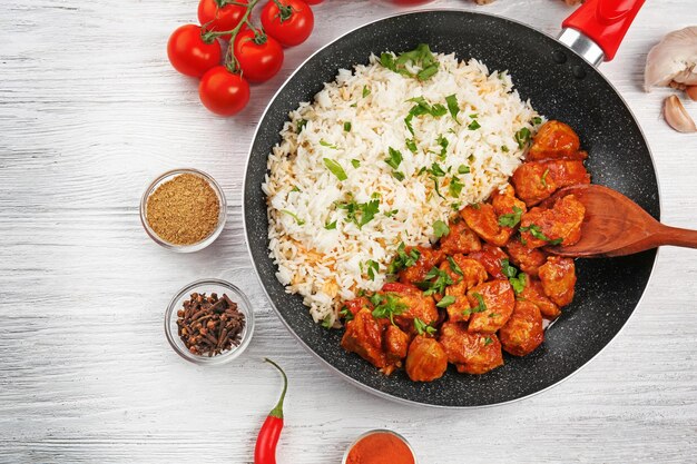 Foto bratpfanne mit leckerem chicken tikka masala und reis auf holztisch