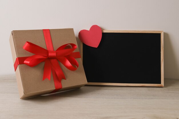 Braune Geschenkbox mit rotem Band und Tafel auf Holztisch.