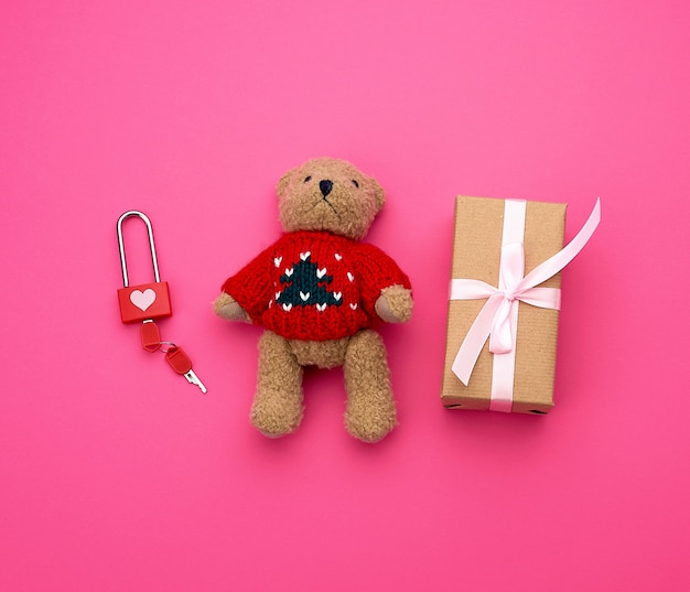 Braune geschenkbox und kleiner brauner teddybär auf einem rosa hintergrund,