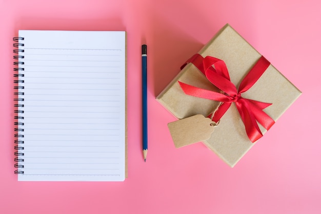 braune Geschenkbox und Notizbuchpapier der Draufsicht auf rosa Pastellfarbhintergrund.