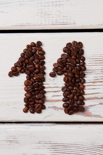 Braune Kaffeebohnen in Form von elf angeordnet. Weiße Holzbretter auf der Oberfläche.