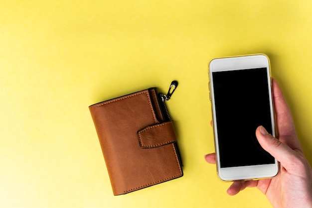 Braune Ledergeldbörse und Handy auf gelbem Hintergrund.