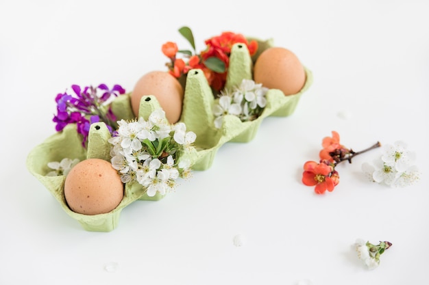 Braune natürliche Eier mit Gesichtern im Tablett, blühende Blumen