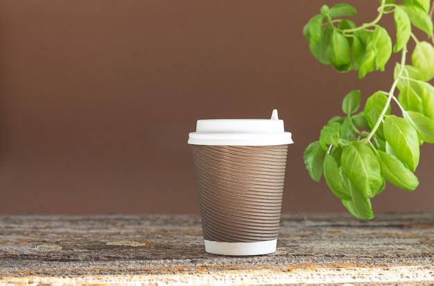 Braune Pappbecher heißen Kaffee auf Holztisch mit Grünpflanze zum Mitnehmen. Café-Tischhintergrund