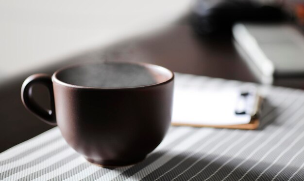 braune Tasse Kaffee mit heißem Dampf auf dem Schreibtisch