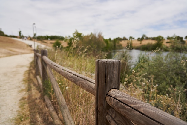 Brauner Holzzaun mit Teich im Hintergrund auf einem Parkweg